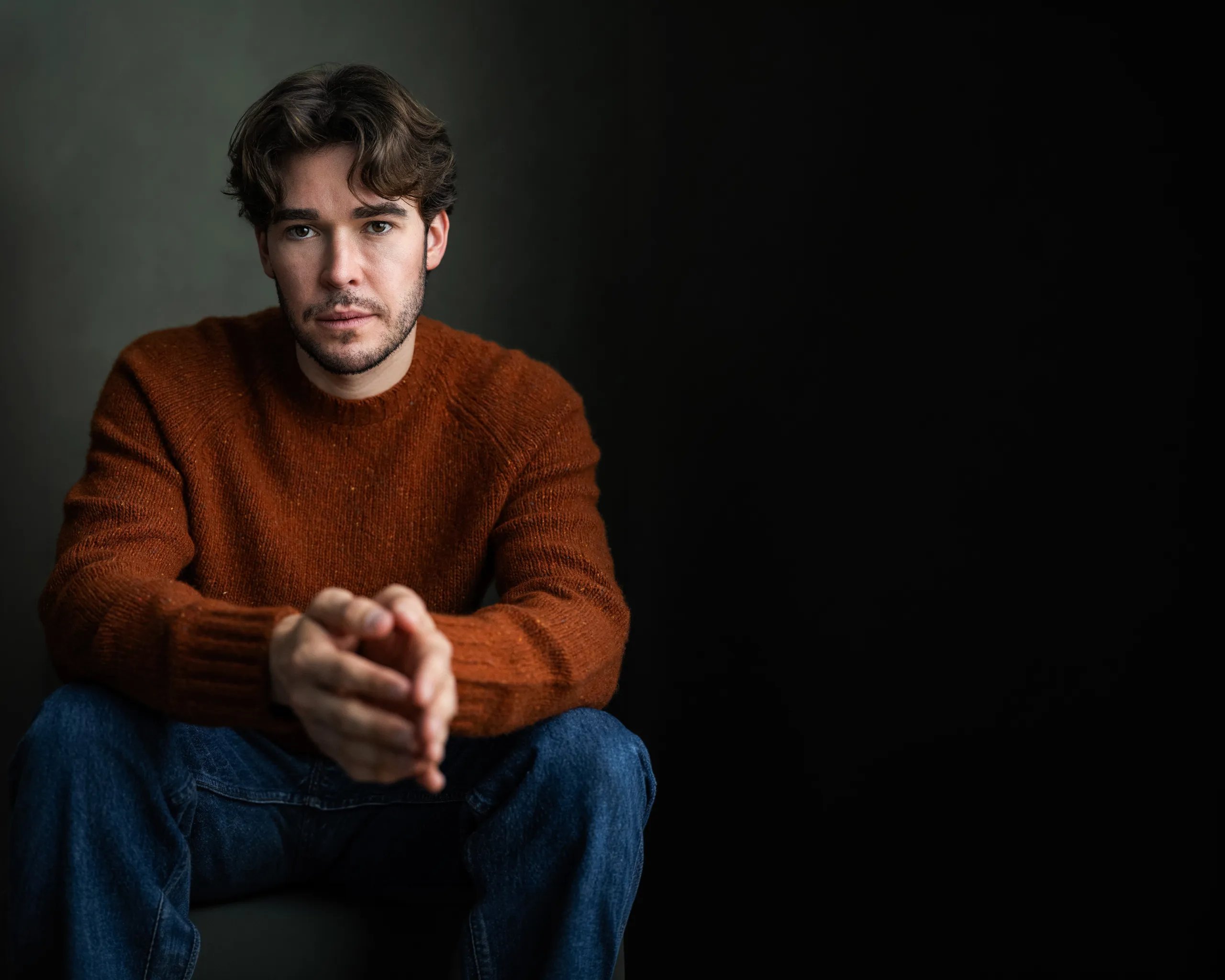 Austin Hammer, seated portrait in a rust wool sweater against a deep green studio backdrop